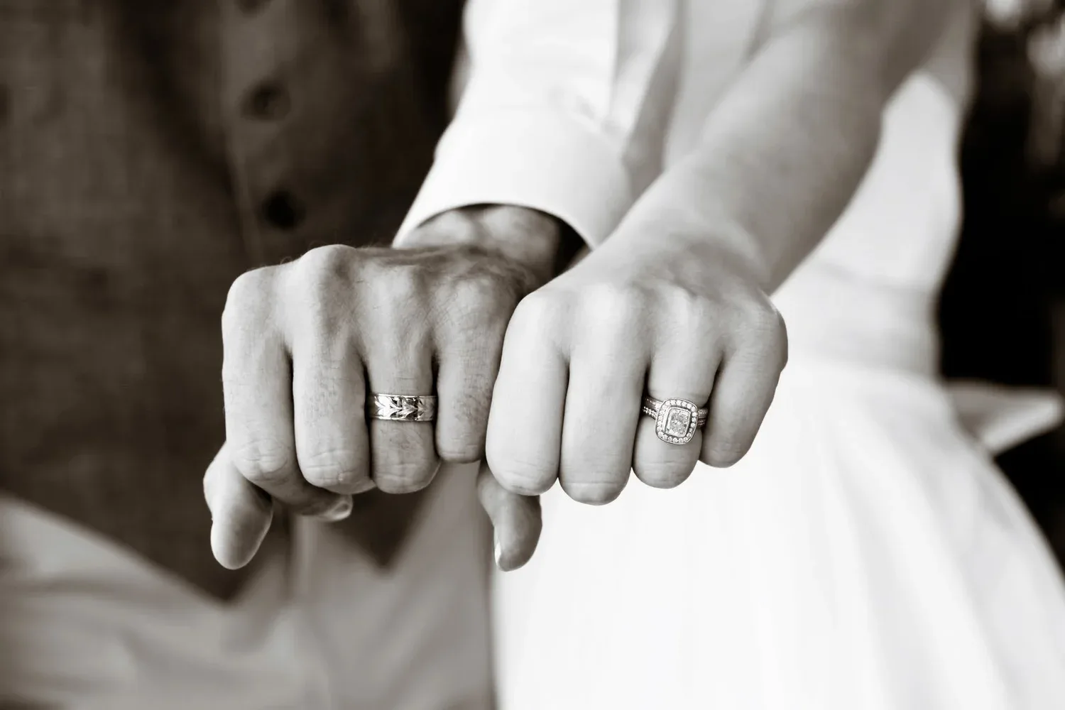 Two clasped hands wearing wedding rings, in black and white